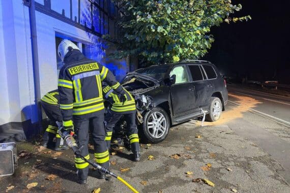 Feuerwehr an Unfallstelle: Pkw prallte gegen Mauer und Baum, Laterne umgeknickt, Brandschutz im Einsatz.