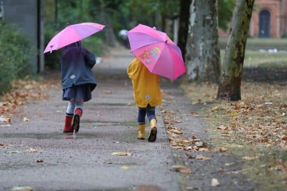Zwei Kleinkinder bei Herbstanfang, im Hintergrund herbstliches Wetter mit Regen und Wolken (Archivfoto).